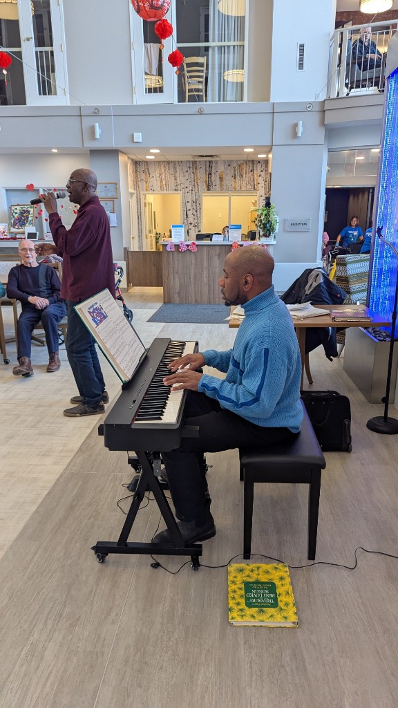 Johnson Philip playing keyboard while a singer performs for residents