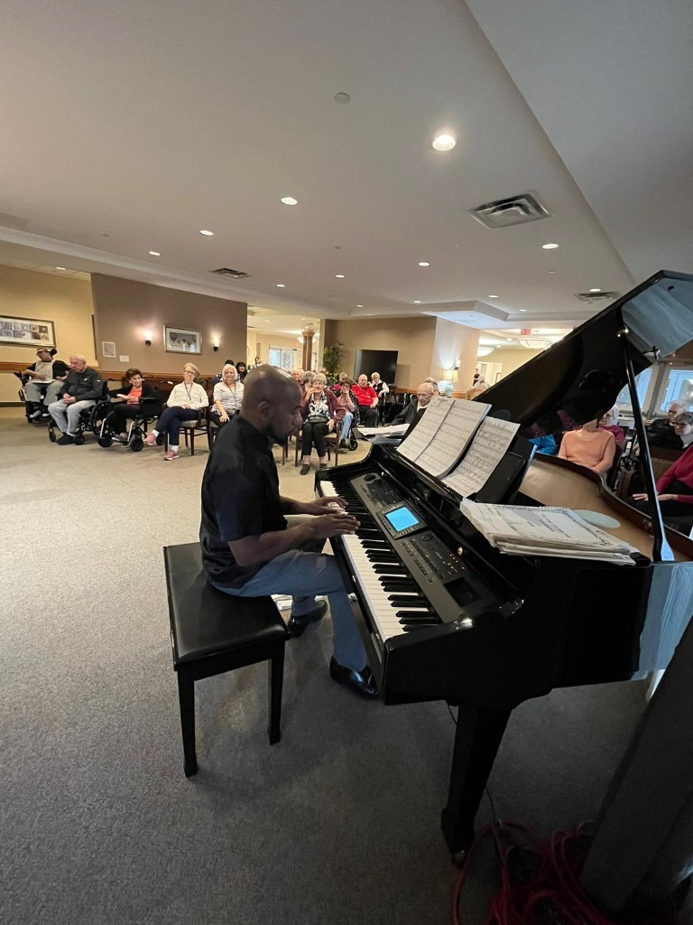 Johnson Philip playing a grand piano for a room of seniors